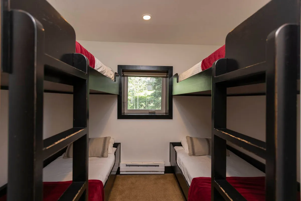A playful bunk room featuring multiple bunk beds and a window, providing a fun and communal sleep space ideal for kids or groups of friends. The room is brightened by natural light and offers a relaxed, social environment.
