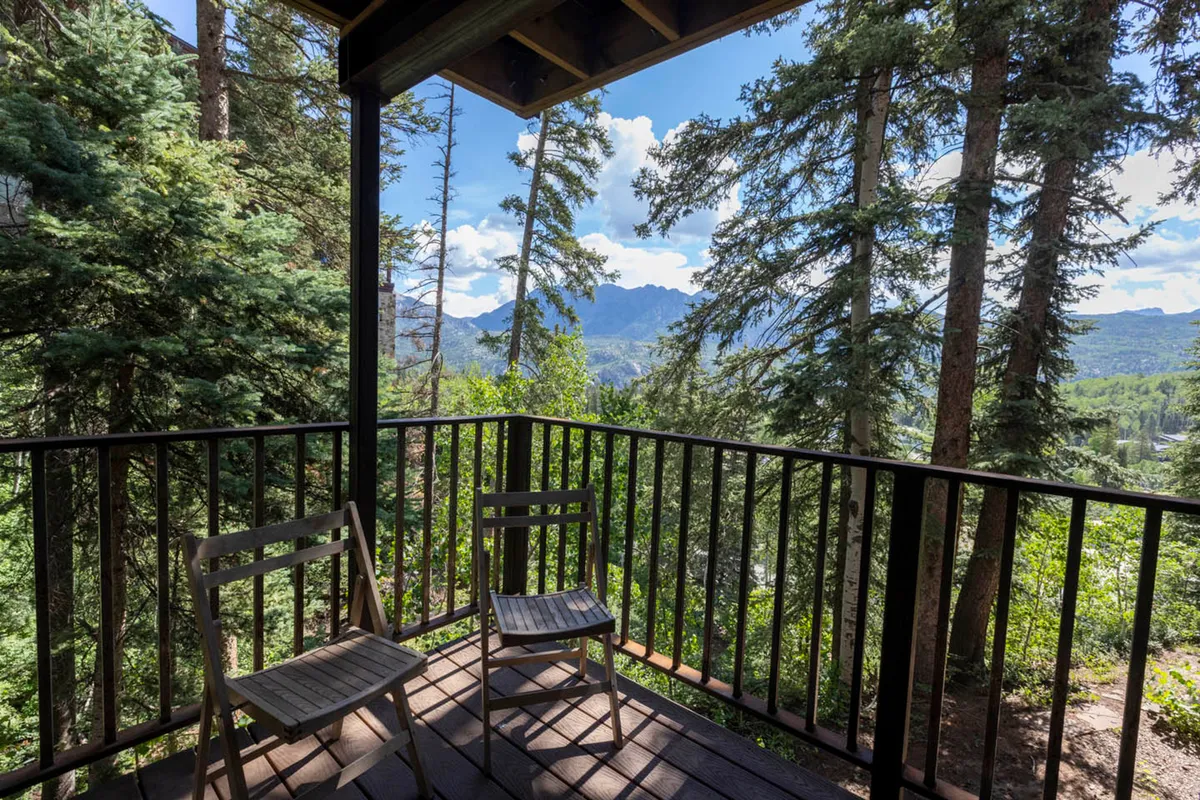 A peaceful exterior shot featuring a private balcony overlooking majestic mountain views and surrounded by tall trees. The balcony invites relaxation, with hints of activities like reading a book or enjoying a warm drink while taking in the sunrise. The tranquil backdrop offers glimpses of wildlife and the promise of starry nights, helping set the mood for family evenings after a day of resort activities.