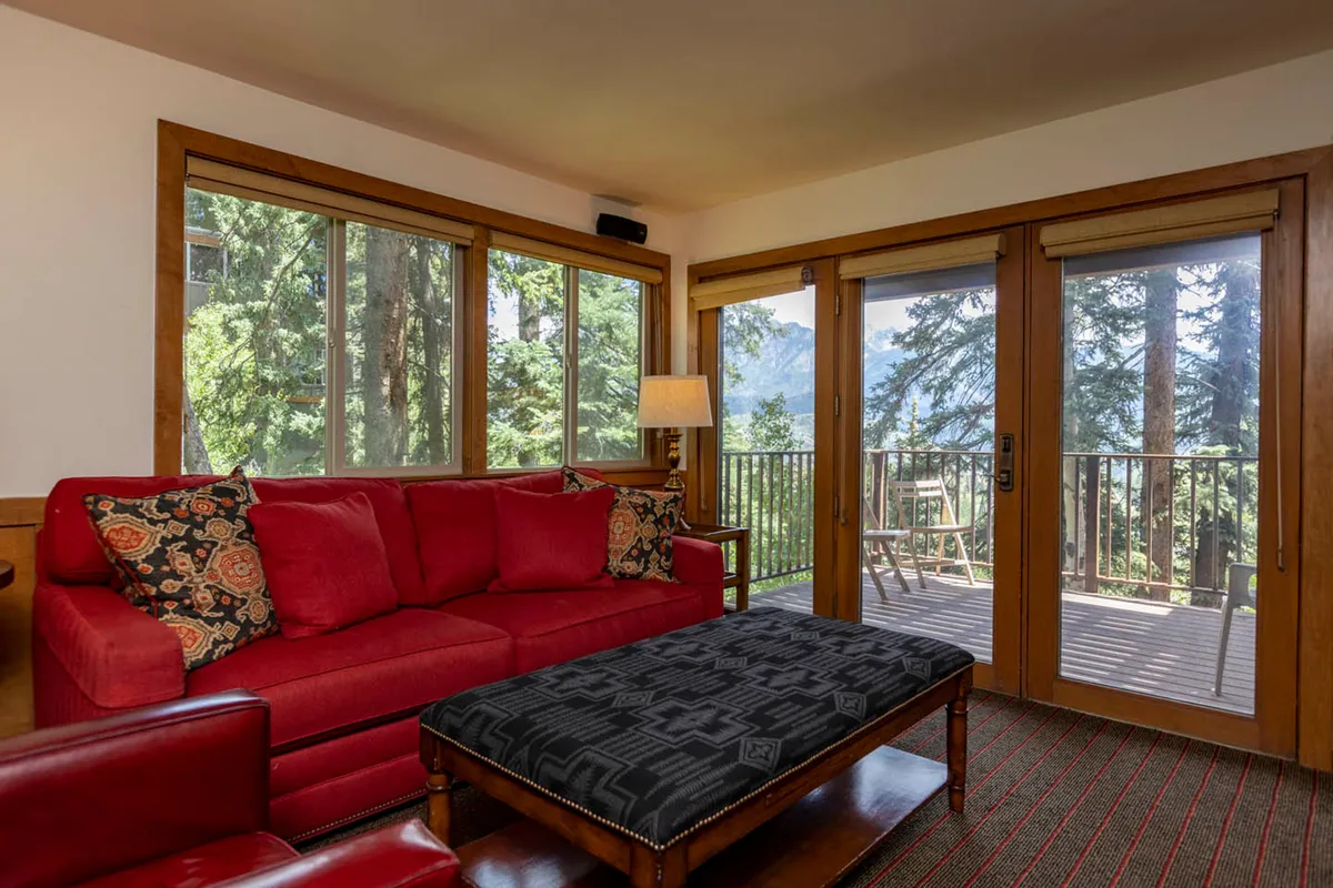 A bright living area with a red sofa, large windows letting in natural light, and a glimpse of the outdoor deck. Decorative cushions and a cozy lamp enhance the inviting mood, making the space ideal for socializing or enjoying the view.