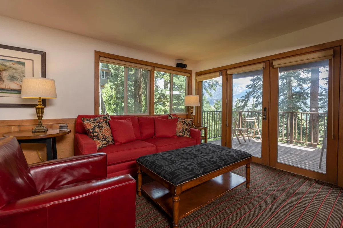 An inviting interior with a plush red sofa, a wooden coffee table, and large windows framing views of the outdoors. Decorative pillows and warm lighting create an atmosphere ideal for group gatherings—whether playing games, sharing stories, or enjoying a quiet, cozy evening together.