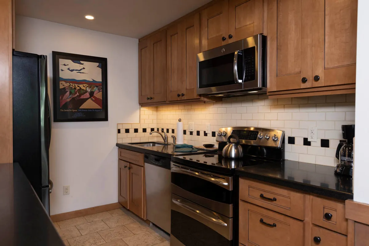 This image showcases a kitchen with stainless steel appliances, a black granite countertop, and attractive artwork on the wall. The space is clearly designed for both cooking and socializing, with modern finishes and thoughtful details that suggest it's ready for group gatherings or family meals.