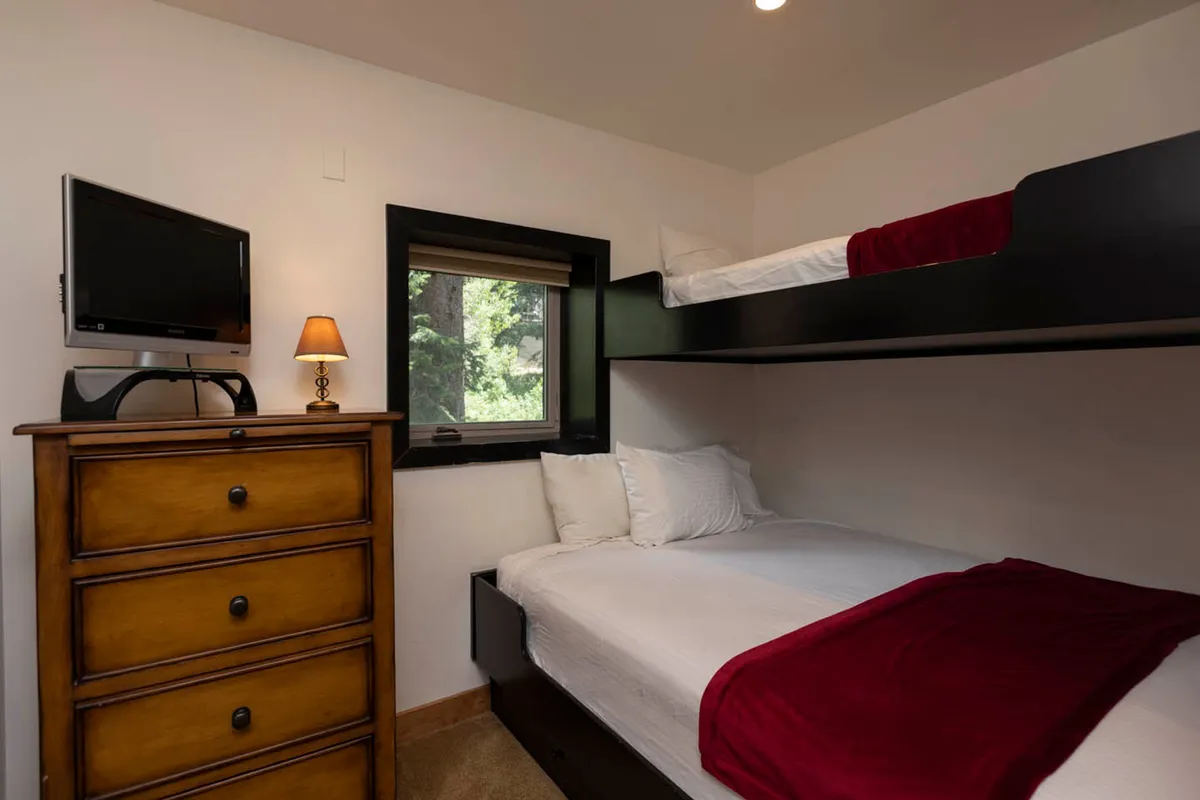 A cozy bedroom with a bunk bed, dresser, window, and lamp, designed for flexibility and comfort. The inviting atmosphere is ideal for siblings, friends, or couples seeking a restful night.