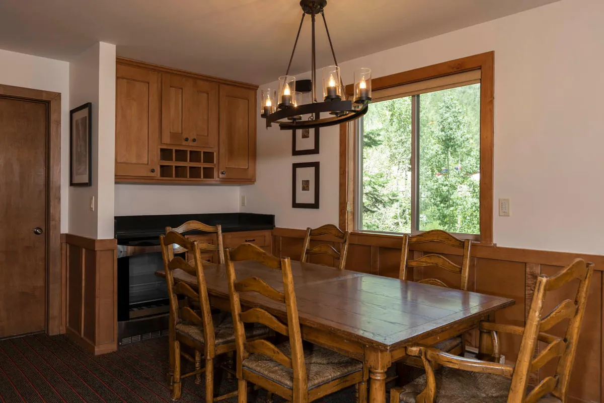 An open dining area with a large wooden dining table set beneath a chandelier, positioned near a window with views of greenery. The space exudes warmth and is perfectly suited for family dinners, celebrations, or casual conversations.